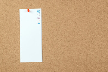 Blank notice with the word ideas printed in vertical on it pinned to a cork board. Copy space.