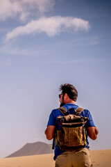Adventure lifestyle with explorer man with backpack viewed from back walking in the desert and...