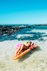Beautiful beach and tropical ocean water with pretty woman lay down on a colorful inflatable mattress lilo relaxing and enjoying the sea nature and the beach in summer holiday vacation
