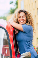 Portrait of happy middle age beautiful woman standing outside her red classic car and smiling to...