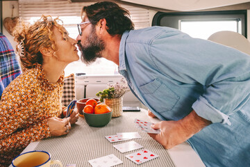 Couple enjoy leisure time playing cards and kissing with love inside a camper van. Travel and...