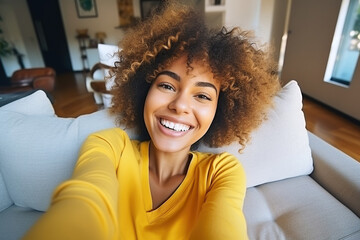 Happy afro American woman relaxing on the sofa at home. Girl taking selfie picture with smartphone - obrazy, fototapety, plakaty