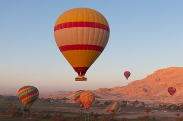 Hot air balloon flying over Hatshepsut Temple at sunrise in Valley of the Kings and red cliffs western bank of Nile river - Luxor- Egypt