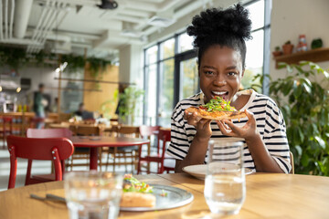 Positive african american woman with a slice of pizza in hands