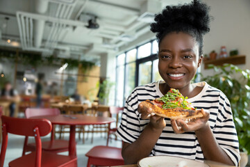 Pretty young dark-skinned woman eating pizza and feeling good