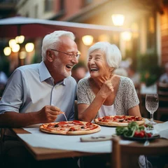 Foto op Canvas Couple of elderly gentlemen with white hair are smiling while eating a pizza. Celebrating anniversary in pizzeria sitting outdoors. Happy people concept © simona