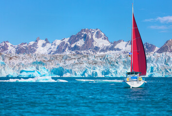 Knud Rasmussen Glacier near Kulusuk with lone yacht and red sails - Greenland, East Greenland