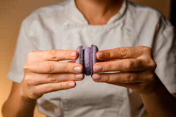 Fototapeta premium Close-up of confectioner's female hands holding together halves of macaroons