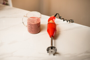 On the kitchen table there is an electric blender and a glass for mixing