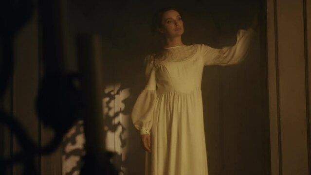 A young woman in a white long dress approaches a colony in a dark Gothic church. Contrasting shadows. Fashion and Cinematic concept