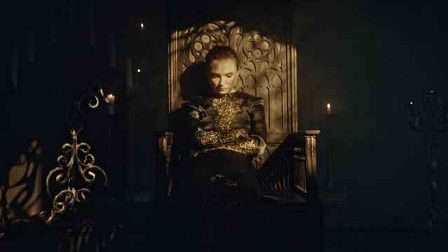A young woman in a black long dress sits in a wooden carved throne in a dark Gothic church. Meditation and expression. Fashion and Cinematic concept
