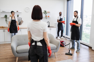 Back view of female boss of cleaning company, telling work schedule to cleaners of studios spacious...