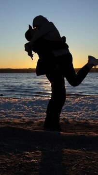 vertical video silhouette couple in love on the seashore at sunset, the man spins the girl holding