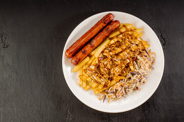 A dish of French fries with bacon, cheese sauce and sausages on a plate