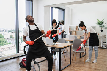 Happy multinational team of people in black aprons cleaning modern office. Professional cleaner...