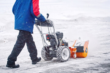 Worker with petrol snow sweeper clean area from snow during blizzard. Worker sweep snow from...