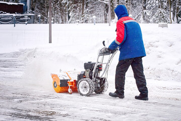 Man with petrol snowblower clean area from snow during blizzard. Worker sweep snow from sidewalk....