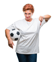 Atrractive senior caucasian redhead woman holding soccer ball over isolated background with angry face, negative sign showing dislike with thumbs down, rejection concept