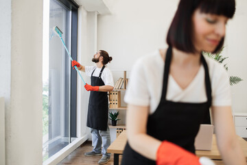 Professional team of people cleaning service in black aprons and red gloves cleans tables, floor,...