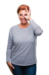 Atrractive senior caucasian redhead woman over isolated background doing ok gesture with hand smiling, eye looking through fingers with happy face.