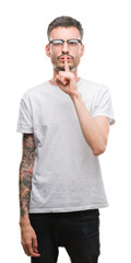 Young tattooed adult man asking to be quiet with finger on lips. Silence and secret concept.