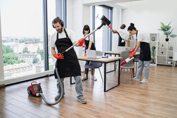 Professional cleaner Caucasian man having fun holding vacuum cleaner like guitar imitating playing...