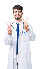 Young doctor man wearing hospital coat over isolated background smiling looking to the camera showing fingers doing victory sign. Number two.