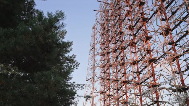 Zoom out Duga radar system view through trees with blue sky on the background in Chernobyl, Ukraine. High quality 4k footage