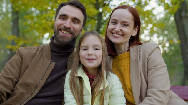 Happy Caucasian family parents mother father daughter child girl kid daughter at autumn park outdoors smiling looking at camera laughing fun together custody adoption bonding holiday at nature laugh