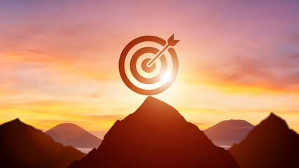 Silhouette target dartboard achievement concept with bullseye on mountain peak at sunrise.
