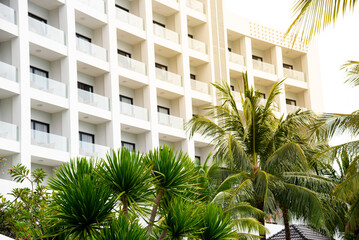 Multistory hotel resort with open glass wall balcony, lush green tall coconut palm trees tropical garden landscape, overcast sky, luxury travel destination in Nha Trang, Vietnam