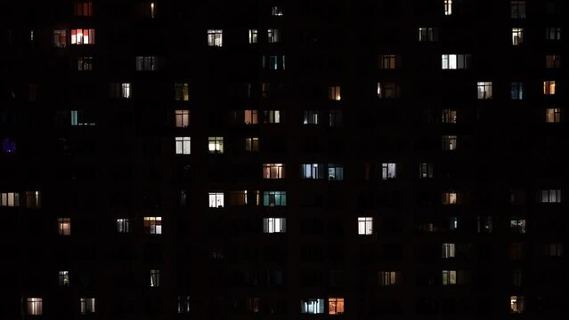 Night time outdoor view of living house facade with light in the windows. Turns on and off the light in the windows apartment building at evening, time lapse. Life in big city, urban concept