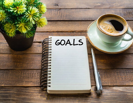 goals list with notebook, coffee cup, plant on wooden table. Resolutions, plan, goals, action, checklist, idea concept