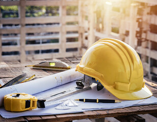 Yellow hard safety helmet hat and the blueprint, pen, ruler, protractor, and tape measure on the table at the construction site.for safety project of workman as engineer or worker