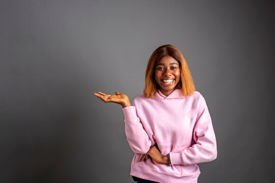 Young Woman Looking At Camera And Smiling While Showing Something Standing On An Isolated Background.