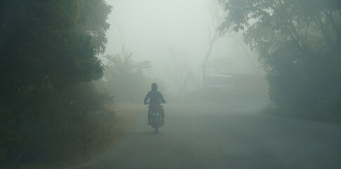 an indian man riding a bike at early morning on foggy road