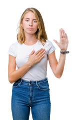 Beautiful young woman wearing casual white t-shirt over isolated background Swearing with hand on...