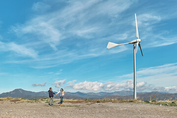 Green energy concept. Couple walking with dog near mountain top industrial wind power plant, wind...