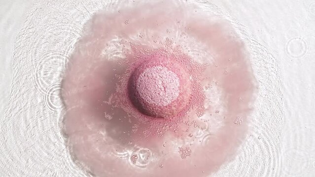 Pink bath bomb ball dissolves in water with white foam bubbles. Cosmetic product natural and skin care. Clear water with reflections sunlight and shadows. . High quality 4k footage