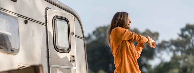 Attractive female feel refreshing and stretching to relax in early morning in front of camper van, motorhome or caravan car trip at park. Camping road trip, freedom vacation, weekend travel or journey