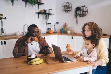 Positive multiracial family sitting at dining table while eating breakfast and having fun at home