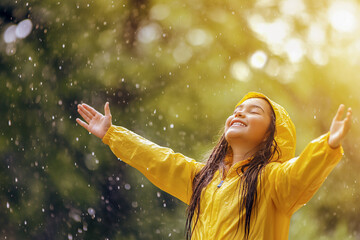 a little girl in a yellow raincoat rejoices while standing in the spring rain