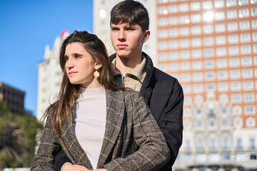 Portrait of a young Caucasian couple in casual clothes embracing with the city in the background.