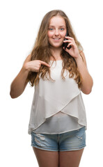 Young blonde woman using smartphone with surprise face pointing finger to himself