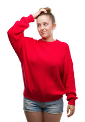 Young blonde woman wearing bun and red sweater confuse and wonder about question. Uncertain with doubt, thinking with hand on head. Pensive concept.