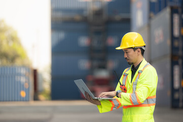 Workers in the import and export industry holding a laptop and standing on the front of container...
