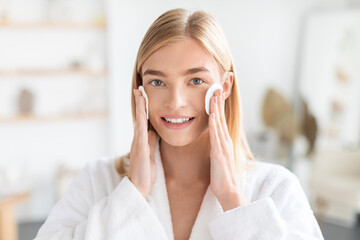 Pretty lady holding cotton pads against her face in bathroom