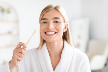 European blonde woman maintaining oral health brushing teeth in bathroom