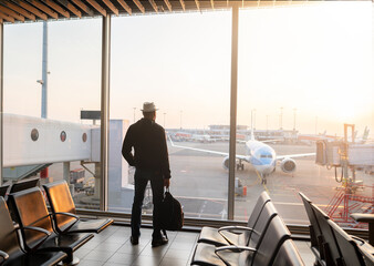Man is standing near window at the airport and watching plane before departure.