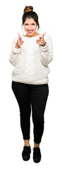 Young beautiful woman wearing winter sweater pointing fingers to camera with happy and funny face....